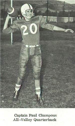 A young white man in a football uniform and helmet holds a football behind his head preparing to throw it
